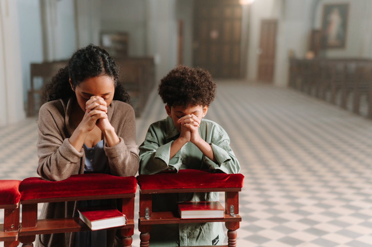 About A mother and son kneeling and praying together inside a serene church.